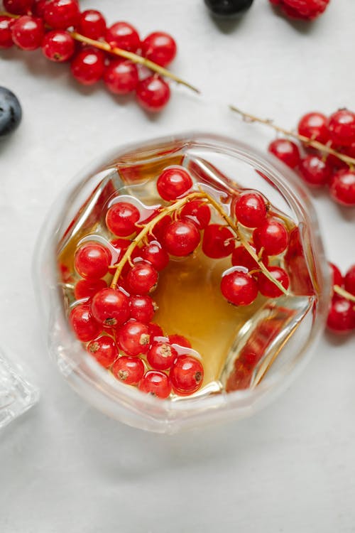 From above composition of branches of red currant berries and crystal drink with berries on white surface
