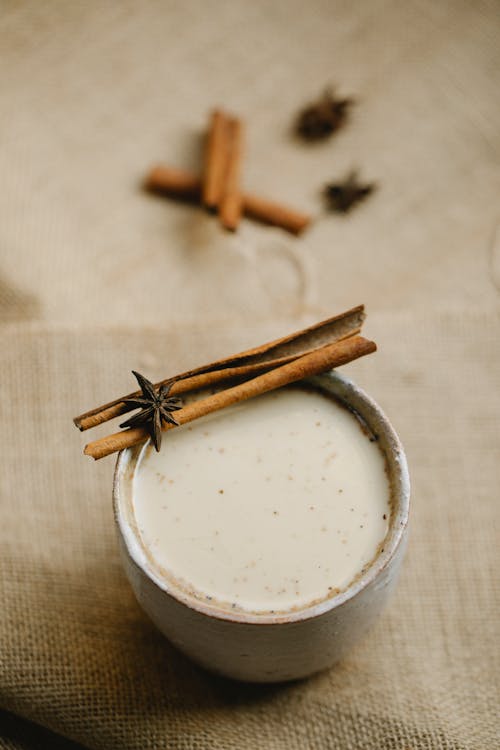 From above cup of spiced traditional milk chai decorated with cinnamon stick and anise stars placed on cloth on blurred background