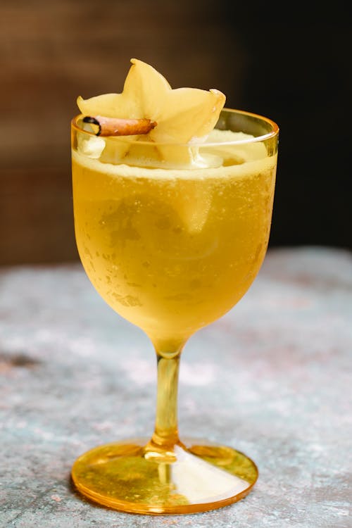 Wineglass filled with fizzy beverage decorated with carambola fruit on cinnamon stick placed on marble table on blurred background in kitchen