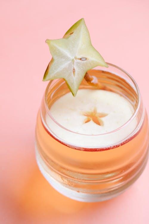 From above of tasty fresh cocktail served with carambola and apple on pink background of studio