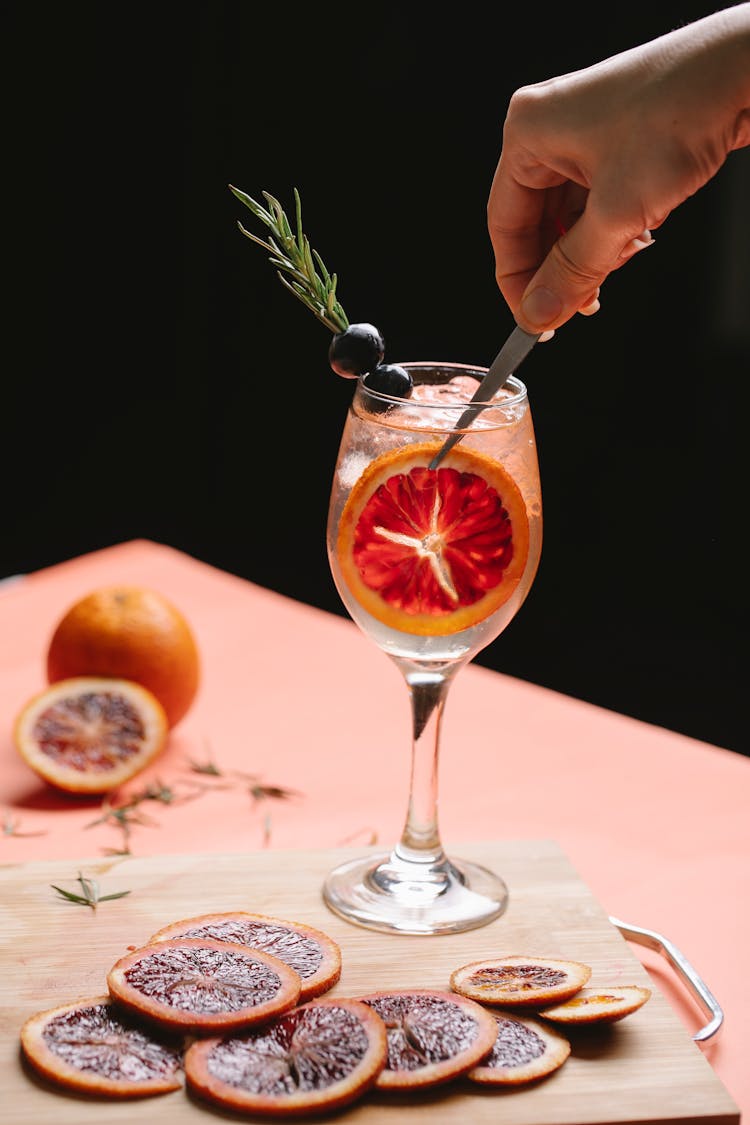 Person Serving Fresh Tasty Cocktail With Red Orange On Table