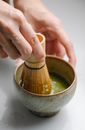 From above of crop anonymous person mixing matcha powder and water with bamboo whisk in ceramic bowl