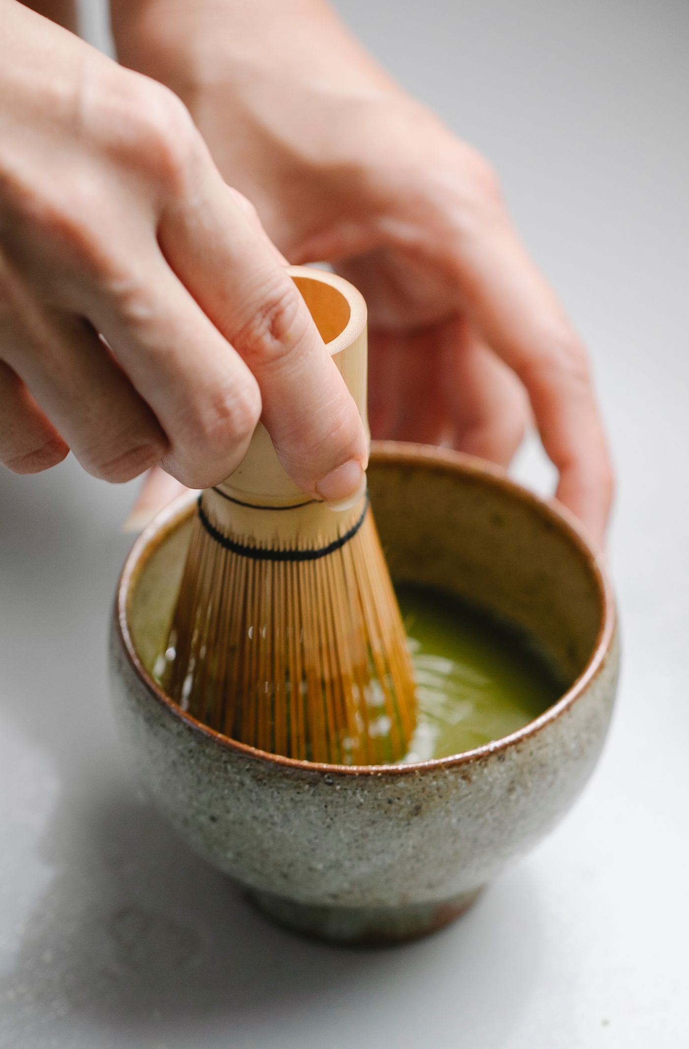 Hands whisking green matcha in a ceramic bowl with a bamboo whisk