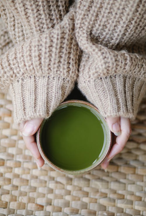Top view of crop anonymous female in soft knitted clothes with hot matcha tea