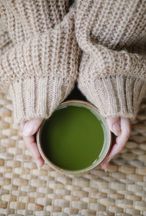 Free Top view of crop Anonymous woman in soft knitted clothes with hot matcha tea Stock Photo