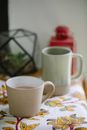 Ceramic mug and cup of fresh tea on oilcloth with floral ornament in house in daytime