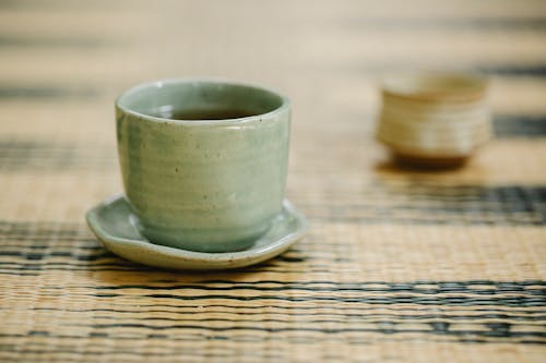 Free Round shaped oriental cups of hot fresh tea with saucer on ornamental mat in daytime Stock Photo