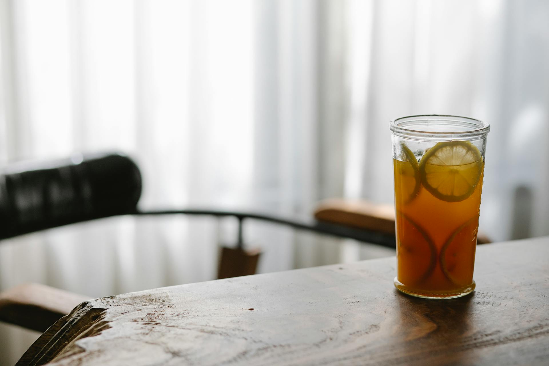 A glass of fresh lemonade with lemon slices on a rustic wooden table indoors, creating a warm and inviting atmosphere.