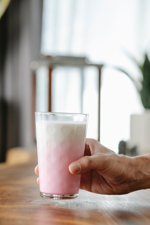 Crop unrecognizable person showing ornamental glass of delicious protein milkshake in house in daylight