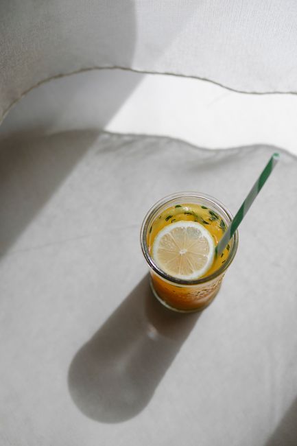 From above of tasty sweet refreshing drink with lemon slice and drinking tube in glass on table with shade