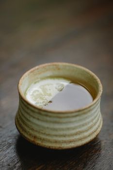 一个装满绿茶的乡村陶瓷杯置于木面之上，呈现出宁静而简约的美感