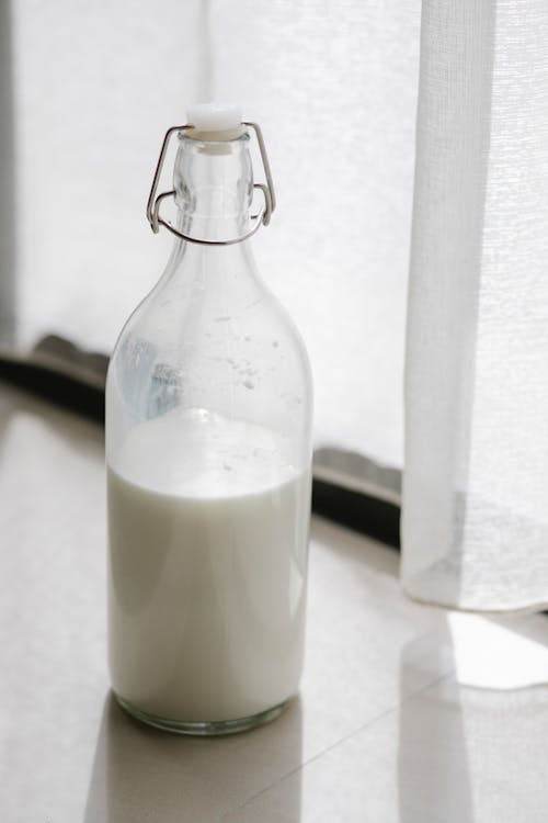 Free Transparent bottle with white creamy milk on windowsill near curtain in house in sunlight Stock Photo