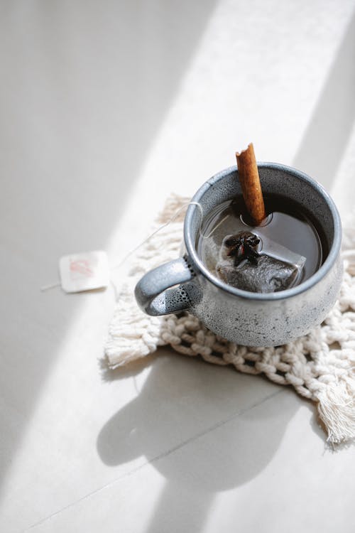 From above of ceramic cup with hot tea with cinnamon stick and anise on knitted napkin