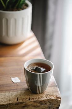 木桌上放着陶瓷杯、热茶和茶袋，杯身有条纹