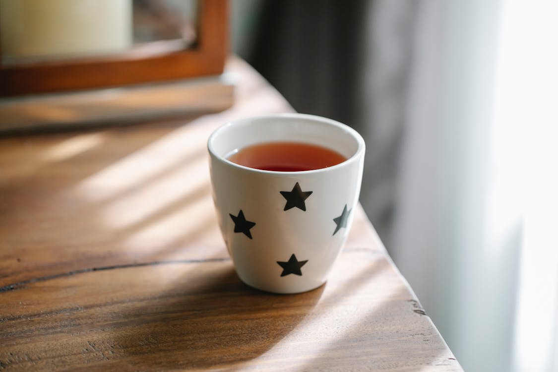 Free High angle of white ceramic cup with stars of hot tasty tea placed on wooden table Stock Photo