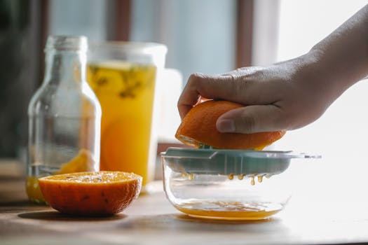Crop anonymous person squeezing half of orange to make homemade juice in kitchen