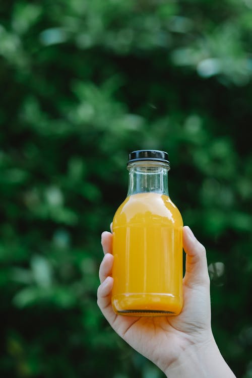 Crop anonymous person showing tasty fresh homemade orange juice in transparent glass bottle