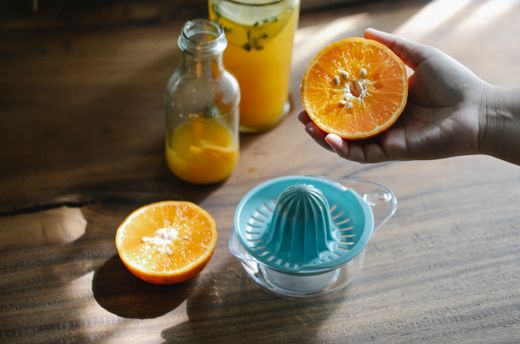 Aqua citrus juicer on glass base beside halved oranges on wood