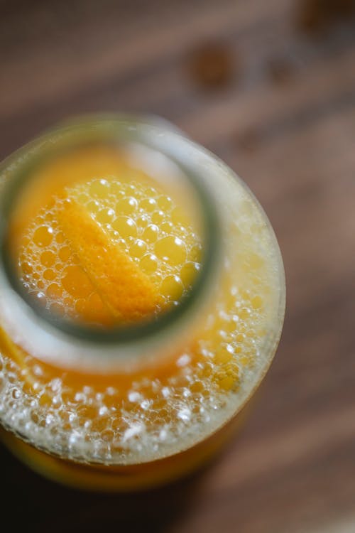 High angle of squeezed orange juice in glass bottle on wooden table at home