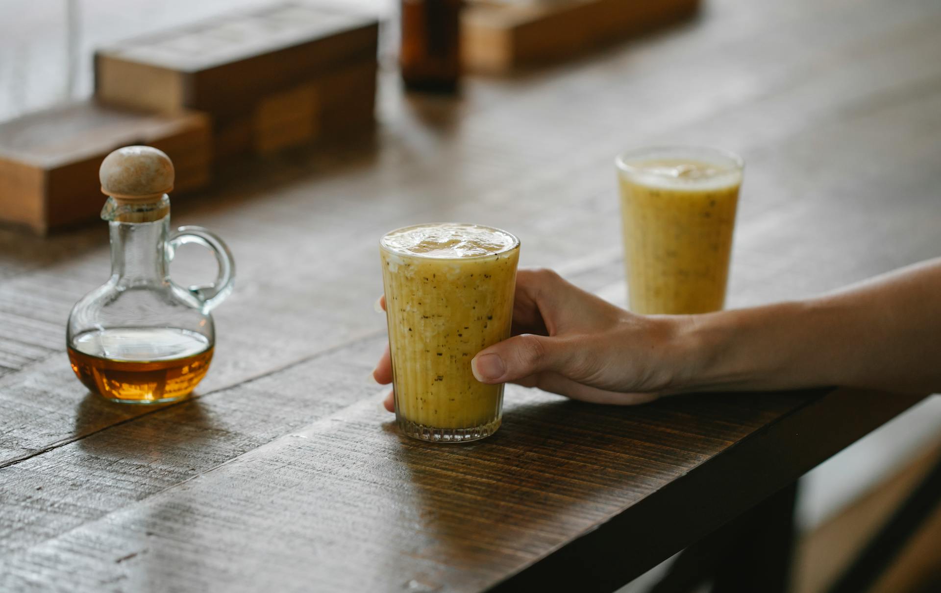 Crop anonymous person sitting at wooden table in modern restaurant and holding glass with fresh healthy smoothie