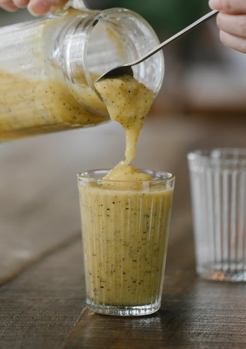 Free Crop unrecognizable person pouring tasty banana smoothie into glass placed on wooden table Stock Photo