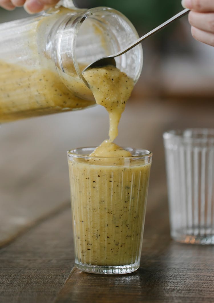 Crop Faceless Person Pouring Fresh Banana Smoothie Into Glass