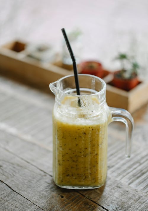 Carafe with fresh healthy banana smoothie with straw served on wooden table in daylight