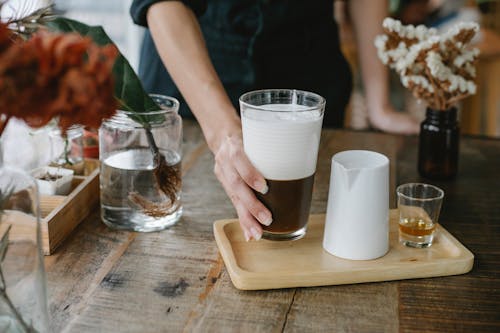 Free Crop anonymous female barista serving fresh brewed iced chocolate coffee with thick layer of fluffy froth on wooden tray with shot of cognac Stock Photo