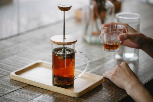Crop anonymous female enjoying aromatic black tea and sitting at table with French press teapot on tray