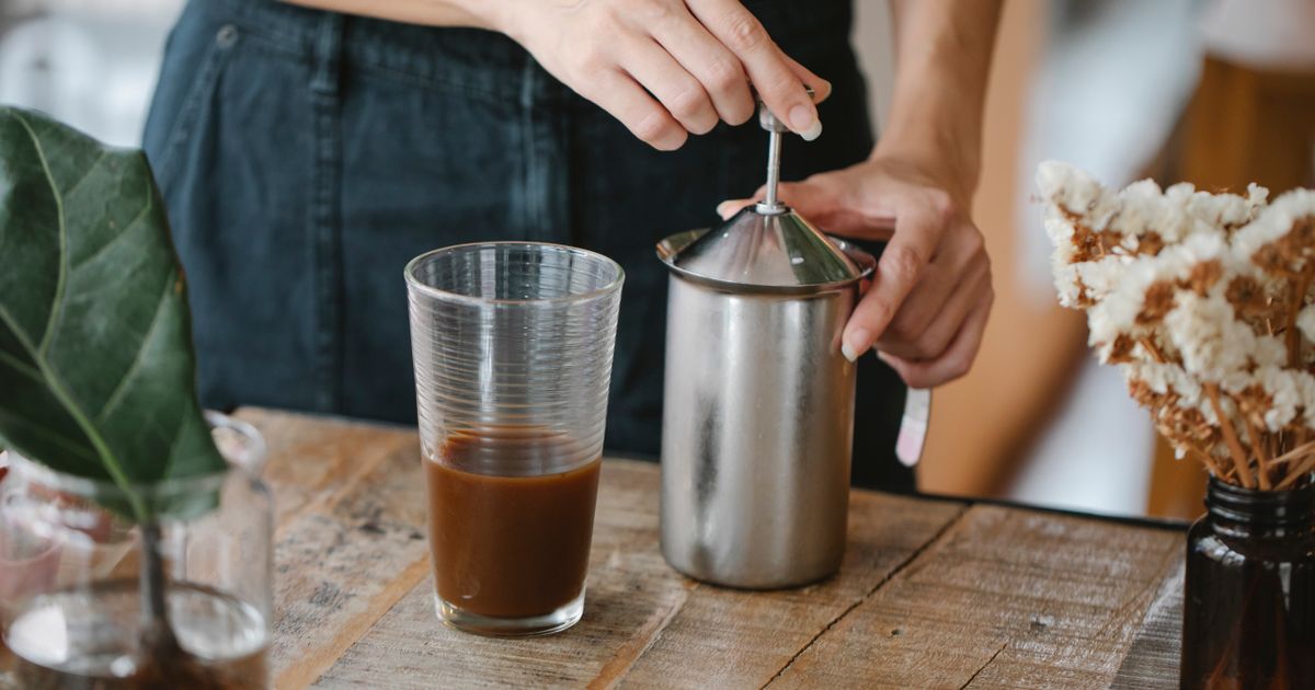 Frothing milk in a steel frother beside a glass of coffee