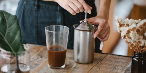 Frothing milk in a steel frother beside a glass of coffee