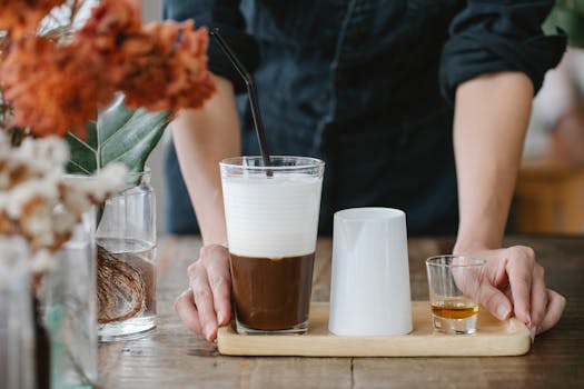 A barista presents a creamy coffee with a small shot of cognac on a wooden tray. by Charlotte May