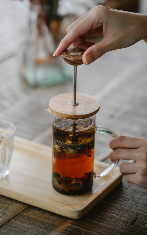 Free Crop anonymous female pressing French press plunger while brewing delicious black tea on wooden tray Stock Photo