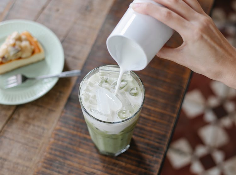 Crop Unrecognizable Woman Adding Milk To Iced Matcha Tea