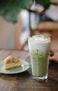 Glass of tasty refreshing matcha latte served on table with yummy pie slice in cafe