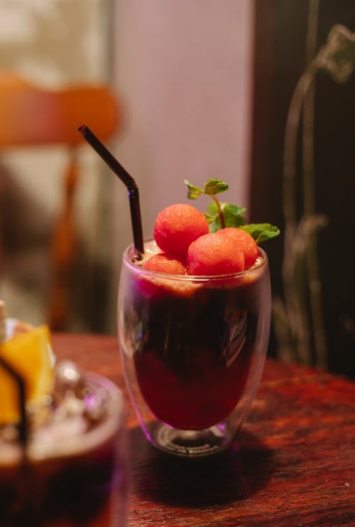 Glass of tasty refreshing mocktail with straw topped with watermelon balls and mint leaf served on table