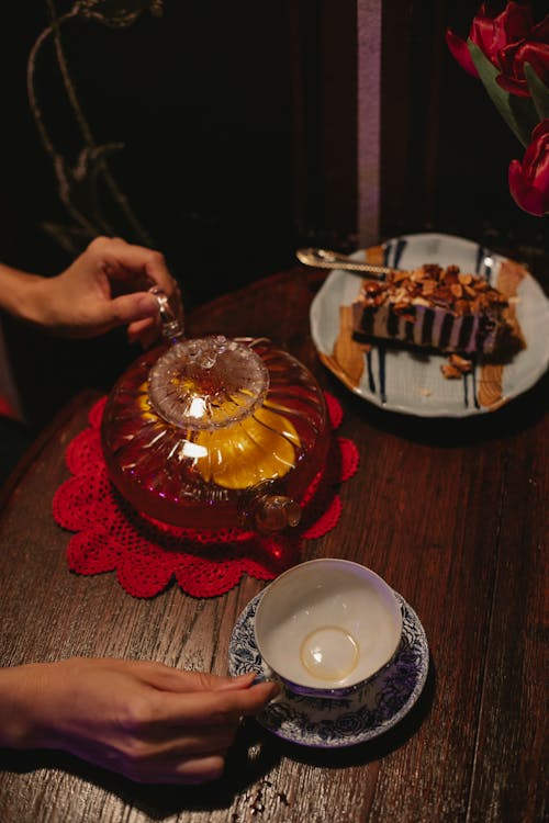 Crop unrecognizable woman touching glass teapot and cup on table