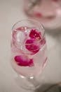 From above glass of refreshing iced water with tender pink rose petals placed on white table