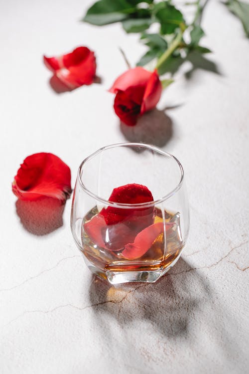 From above of transparent glass with red rose petals and alcoholic drink near rose flower