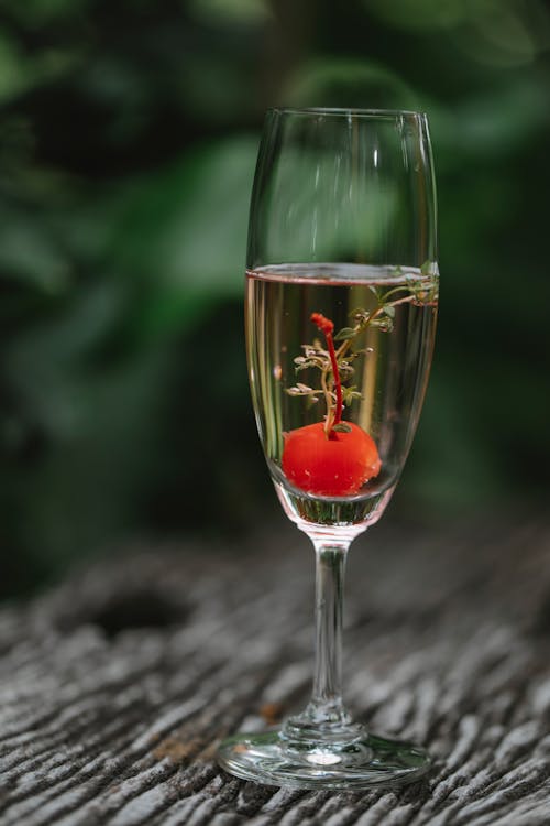 Crystal glass of alcoholic cocktail with cherry and mint on wooden table against blurred background