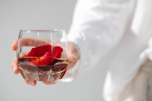Elegant glass of whiskey with rose petals held by a hand, perfect for romantic occasions.