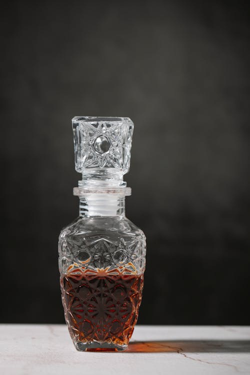 Crystal transparent decanter with whiskey placed on table in studio against black background