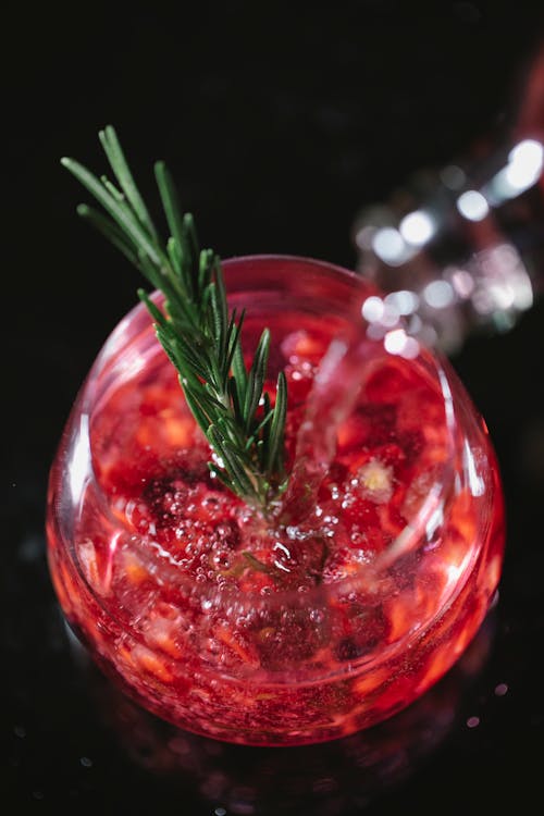 From above of crystal glass of pomegranate champagne cocktail served with rosemary sprig on black table