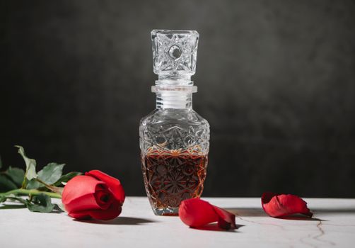 深色威士忌注满了水晶倾析器，周围点缀着红色的玫瑰与花瓣