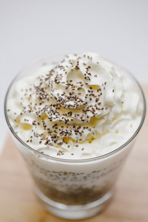 From above of glass of delicious dessert with whipped cream and chia seeds placed on wooden surface