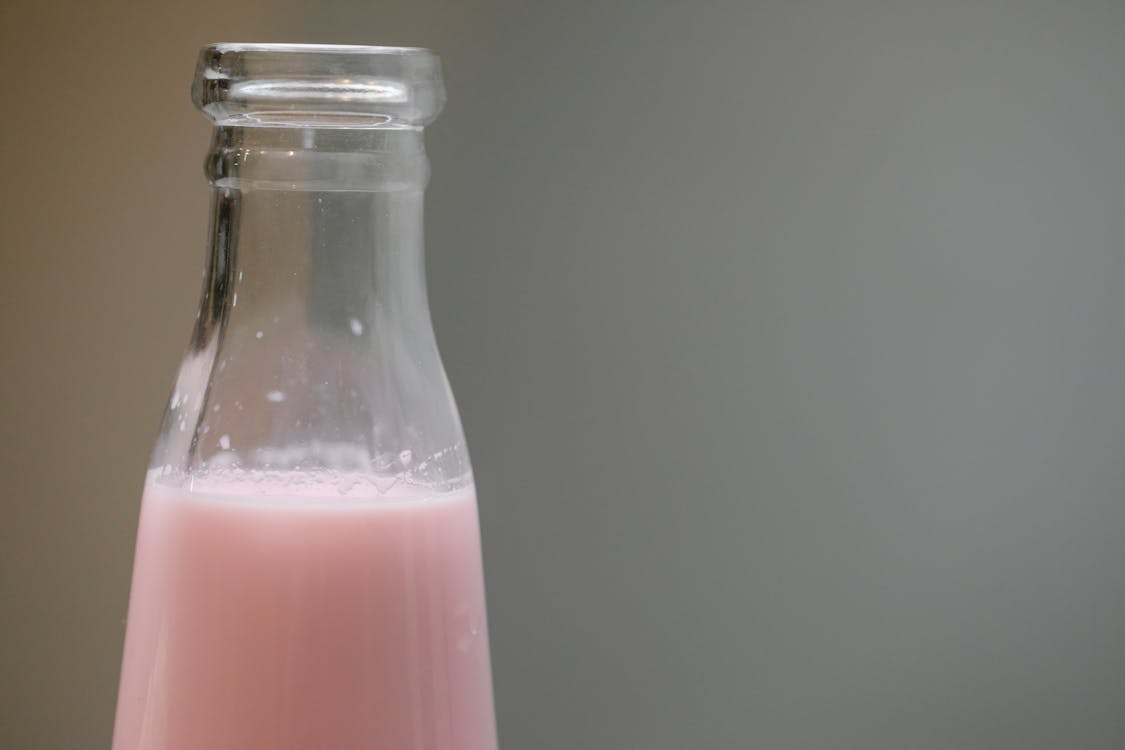 Glass bottle with tasty pink milk shake placed in room against blurred gray background