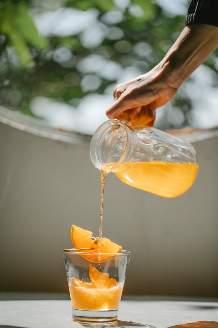 Crop Woman Pouring Cold Orange Beverage Into Glass