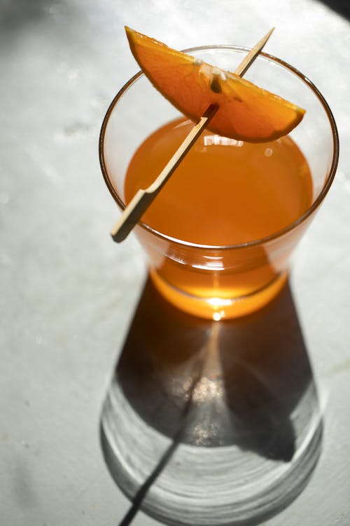 Glass of orange alcohol cocktail with sliced orange on stick