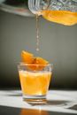 Nonalcoholic drink poured from crystal jar into transparent glass decorated with piece of orange on thin wooden stick
