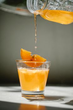 将非酒精饮料从水晶罐倒入透明玻璃杯，并用细木棍装饰以橙色